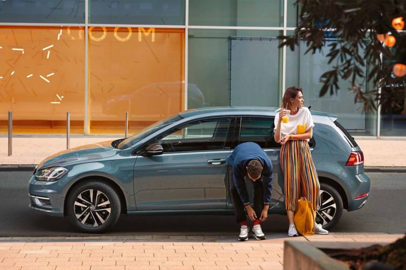 Un ragazzo e una ragazza appoggiati alla fiancata di un'auto Volkswagen, vista lateralmente.