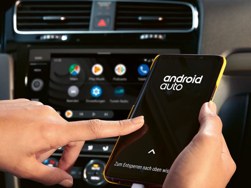 Una mano usa un cellulare collegato con logo Android Auto all’interno di una Volkswagen
