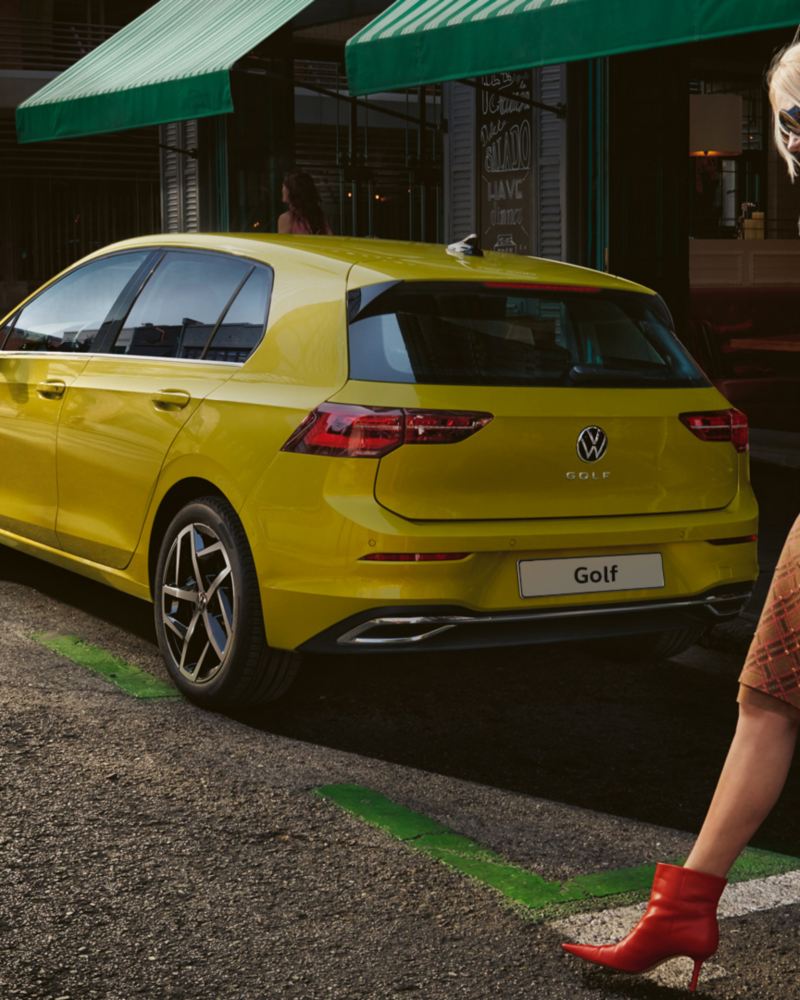 Una donna passeggia di fianco ad un'auto Volkswagen Golf 8