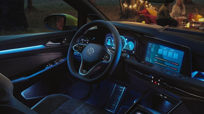 Interiøret i en VW Golf med blik på rattet og displayet med indstilling af den aktiverede ambientebelysning, der er blåt lys i interiøret.