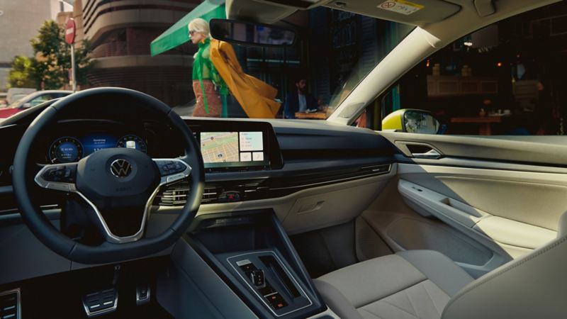 Interior of the VW Golf with the steering wheel and optional Innovision Cockpit, view of an urban landscape through the windscreen.