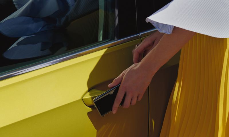 Eine Frau nutzt ihr Smartphone als mobilen Schlüssel und öffnet damit die Tür eines VW Golf.