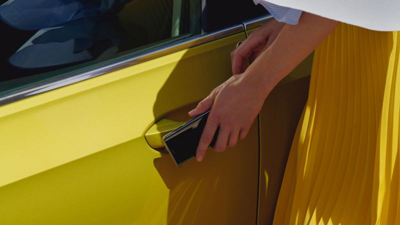 A woman uses her smartphone as a mobile key to open the door of a VW Golf.