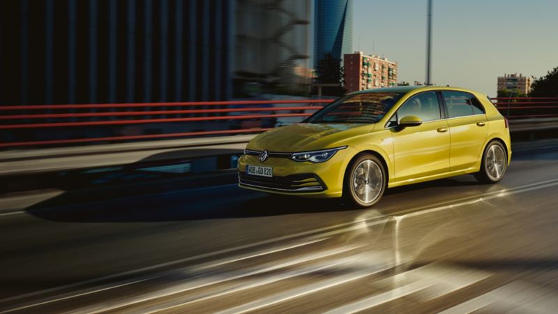 Une Golf jaune en mouvement sur la route. Vue avant et profil.