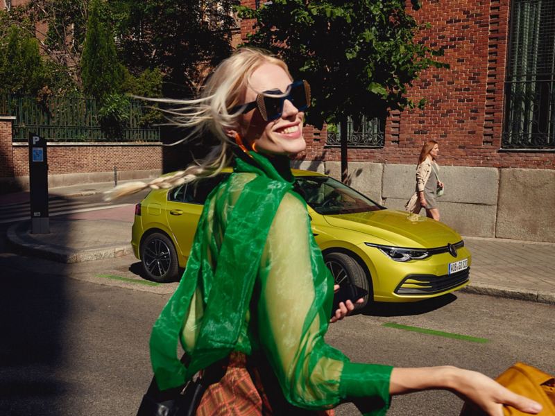 En kvinne står foran Volkswagen Golf kompaktbil og smiler