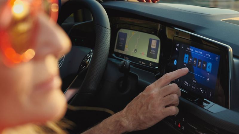 Un couple dans la VW Golf, le conducteur manipule l'écran tactile pour sélectionner ses préférences de confort.