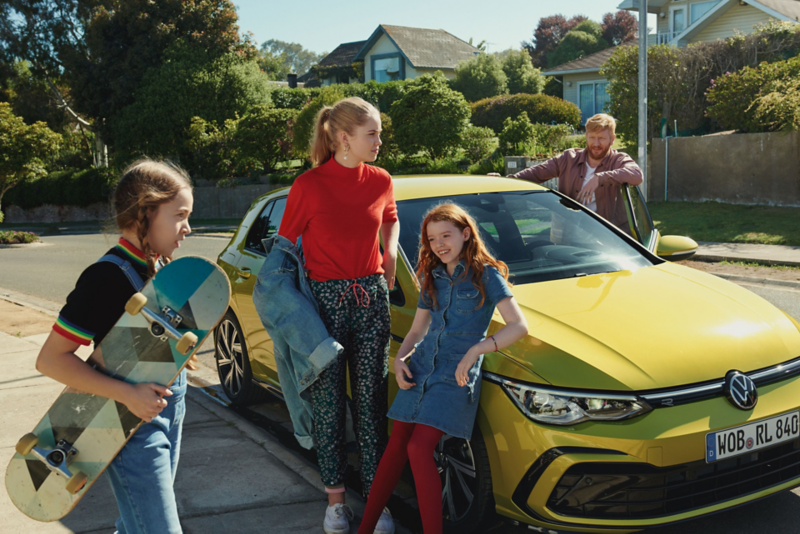 Une famille devant une Golf 8 jaune avec la porte conducteur ouverte.