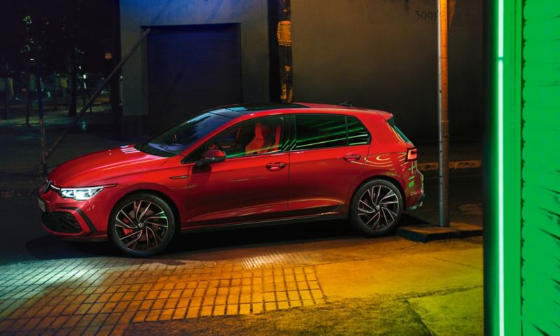 VW Golf GTI rouge, vue latérale, phares IQ.Light lumineux en option et projection lumineuse des rétroviseurs extérieurs au sol.