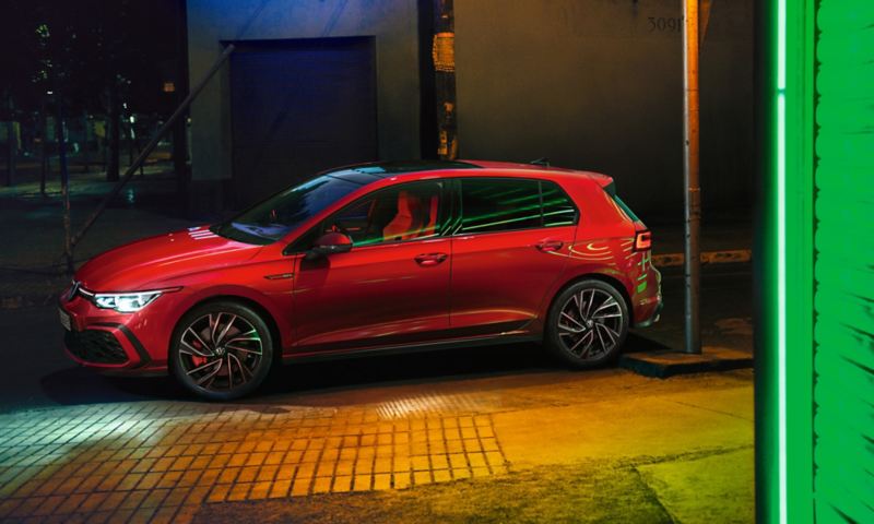 Red VW Golf GTI, side view with optional IQ.LIGHT headlights switched on and projection of light onto the ground from the exterior mirror
