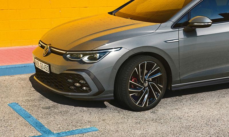 Γκρι VW Golf GTD μπροστά από έναν κίτρινο τοίχο σε ένα χώρο στάθμευσης αυτοκινήτων. Λήψη από το πλάι, τους τροχούς και τους προβολείς.