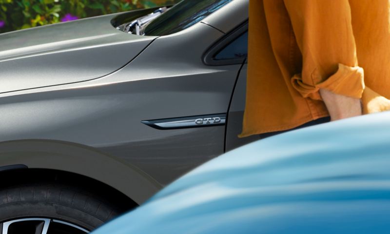Volkswagen Golf GTD con messa a fuoco sull’emblema sul lato del cofano; davanti, quasi fuori dall’immagine, una persona con una camicia arancione.