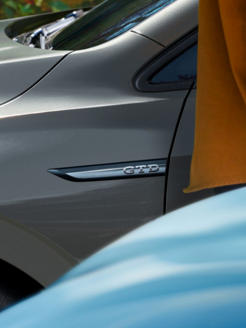 La VW Golf GTD met l’accent sur le badge sur le côté du capot, devant une personne portant un t-shirt orange presque hors de l’image.