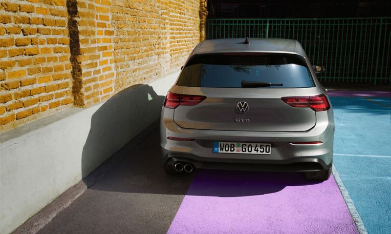 Vue arrière sur l’extérieur d’une VW Golf GTD sur un terrain de sport à côté d’un mur de briques.