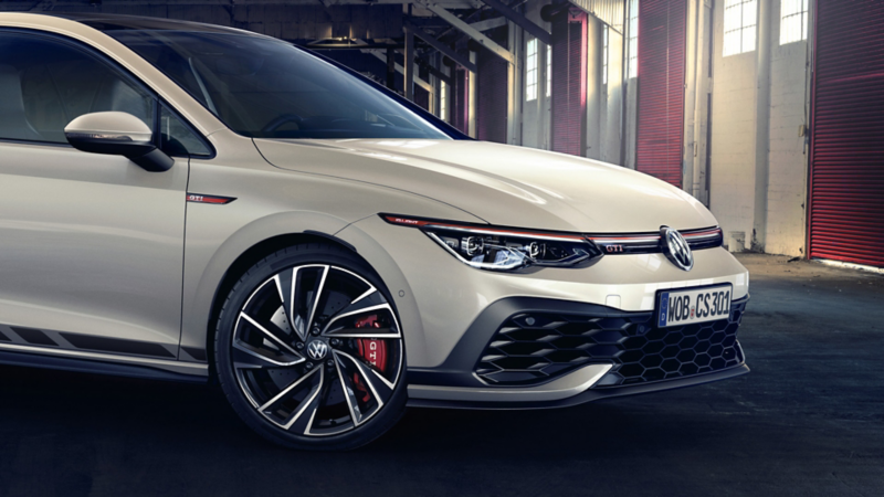 View of the front to the passenger door of a parked white VW Golf GTI Clubsport. View of the wheel rim and headlights. 