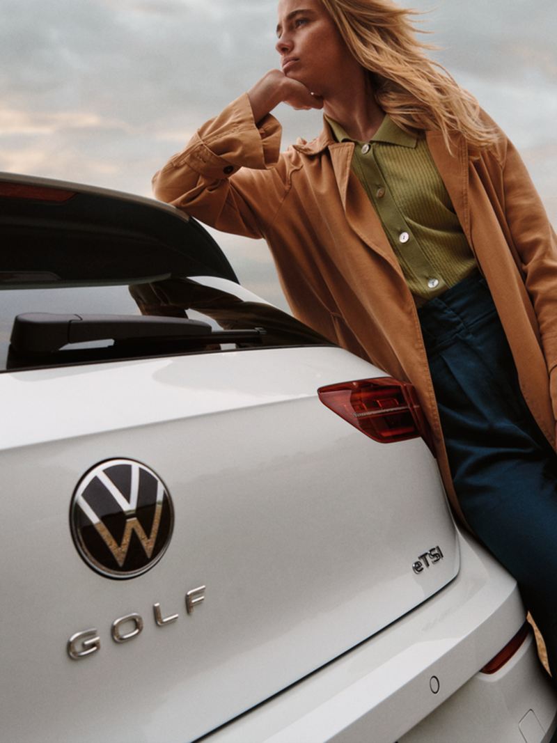 Una ragazza appoggiata alla sua Volkswagen Golf 8 eTSi, vista posteriormente con dettaglio sul badge.