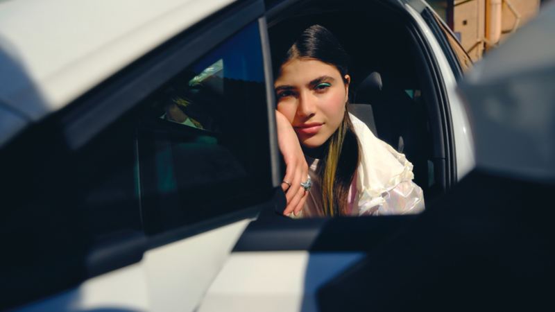 Frau sitzt auf Fahrersitz eines VW Golf GTE und schaut auf dem Lenkrad lehnend aus der geöffneten Fahrertür in die Kamera.