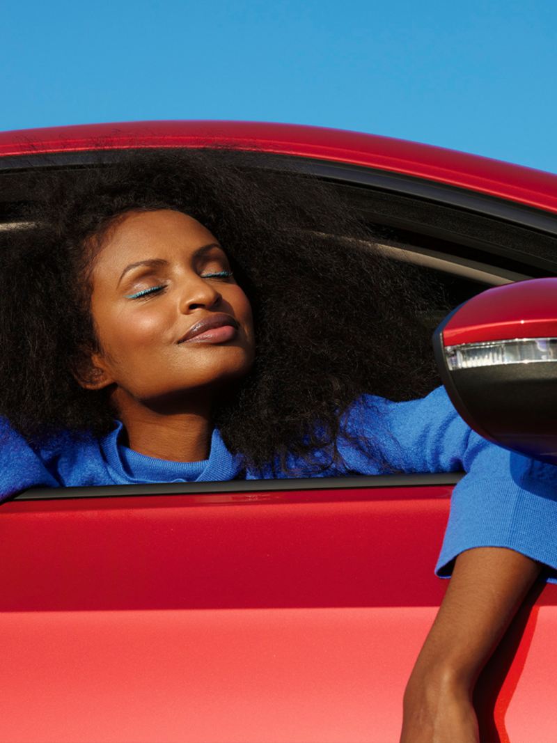 Une VW Golf rouge avec une fenêtre ouverte. Une femme en pull bleu se penche vers l'extérieur.