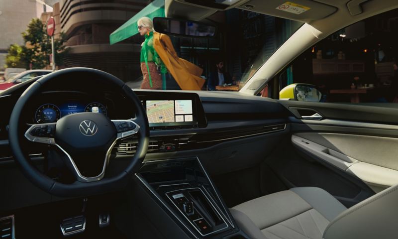 Interno di VW Golf 8 con volante e Innovision Cockpit opzionale, vista di un paesaggio urbano attraverso il parabrezza. 