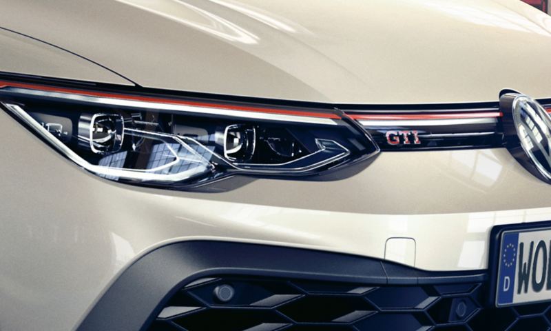 Detailansicht der Front eines weißen VW Golf GTI Clubsport, mit Fokus auf einen LED-Scheinwerfer und dem GTI Schriftzug im Kühlergrill. 