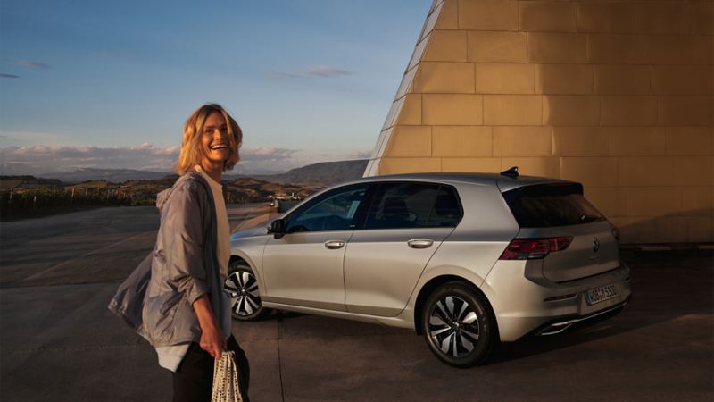 En kvinne står foran en VW og ler