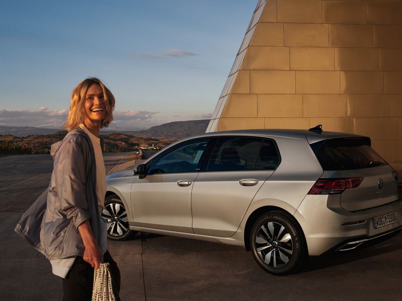 Uśmiechająca się kobieta stojąca przed swoim Volkswagenem