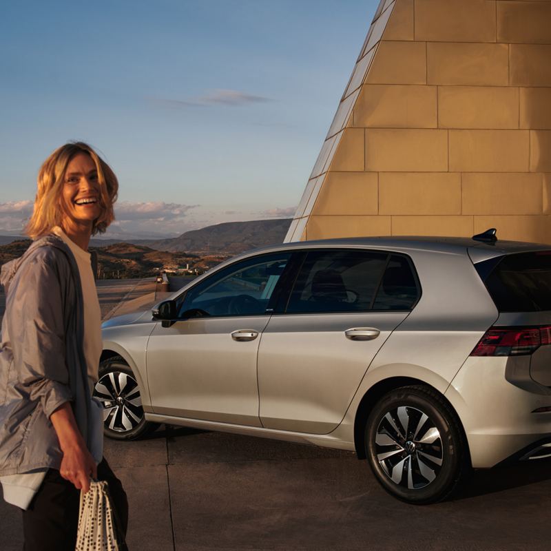 Moteris stovi priešais „Volkswagen“ ir juokiasi
