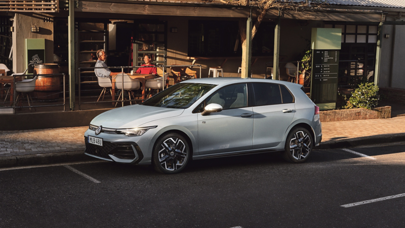 En vit VW Golf står parkerad längs vägen utanför ett café