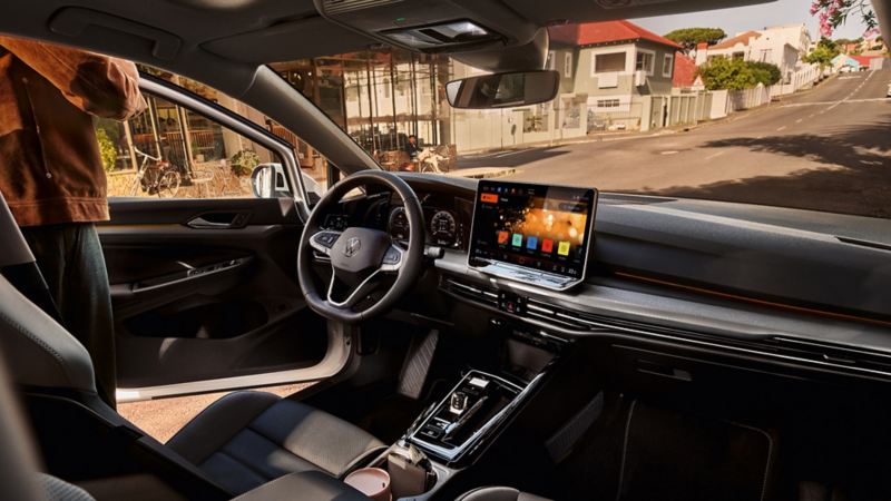"Habitacle de la VW Golf avec une personne au volant : vue sur l’éclairage d’ambiance en violet et sur le grand écran. "