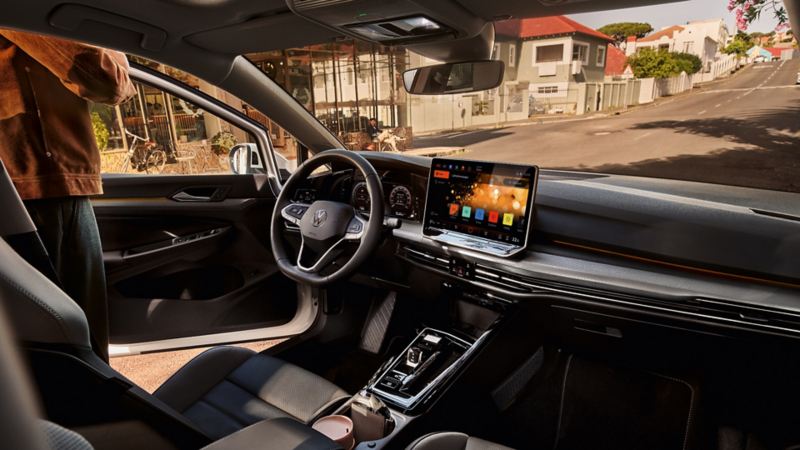 "Nowy Golf GTI w kolorze czerwonym, zaparkowany przed garażem. Osoba stoi za samochodem i patrzy na smartfon. "