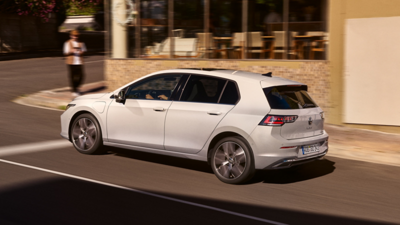 White VW Golf driving on the street next to a restaurant.