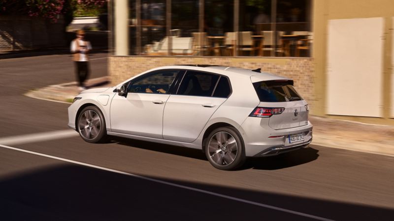 "Een witte VW Golf rijdt op de weg langs een restaurant. "