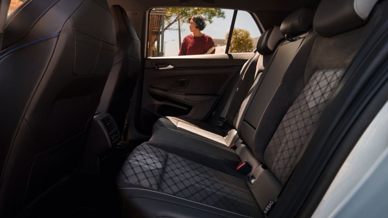 Interior view of the rear bench seat in the VW Golf. A woman can be seen through the window. 