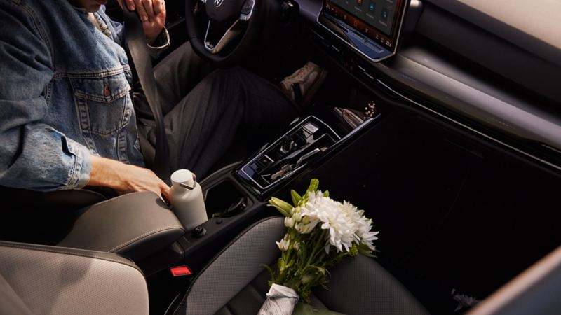 Innenansicht des VW Golf mit Fokus auf die Mittelkonsole und dem Beifahrersitz, auf dem sich Blumen und eine kleine Tasche befinden. Eine Person sitzt auf dem Fahrersitz.