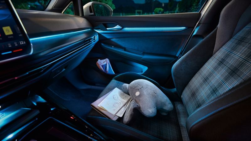 Intérieur d'une Golf GTE illuminé par l'éclairage d'ambiance. Une peluche et des dessins d'enfants sont posé sur le siège avant passager.