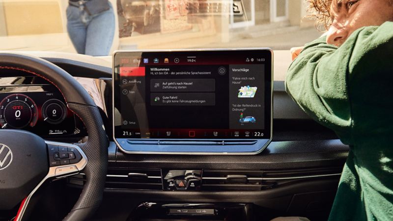 Blick auf das Infotainmentsystem eines VW Golf GTI mit Mann auf dem Beifahrersitz.