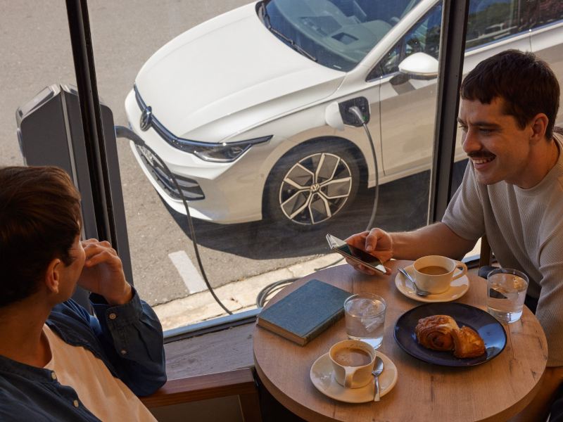 A couple sits in a café as a Golf charges on the street outside