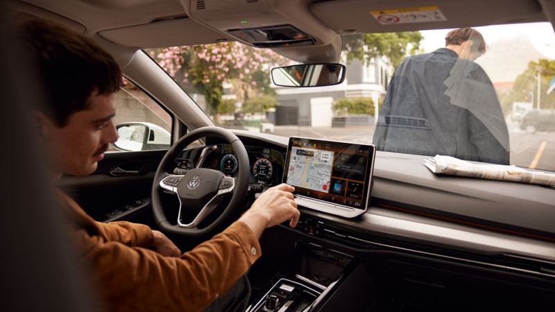 Innenansicht des VW Golf mit Fokus auf die Web Radio Anzeige auf dem großen Bildschirm. Ein Mann sitzt auf dem Beifahrersitz und blickt lächelnd in Richtung des Fahrersitzes. 
