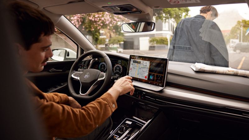 "Interieur van de VW Golf met focus op de webradio-weergave op het grote scherm. Een man zit op de passagiersstoel vooraan en kijkt lachend in de richting van de bestuurdersstoel. "