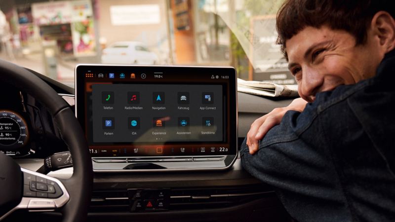 Innenansicht des VW Golf mit Fokus auf die Web Radio Anzeige auf dem grossen Bildschirm. Ein Mann sitzt auf dem Beifahrersitz und blickt lächelnd in Richtung des Fahrersitzes.