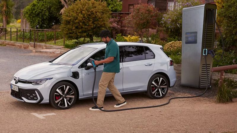 Un homme recharge une Golf GTE blanche sur une borne de recharge DC.