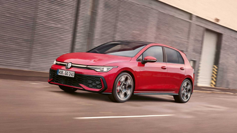 a red VW Golf GTI Clubsport driving along a road with grey building behind it