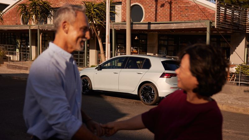 Un couple se tient la main devant une VW Golf.