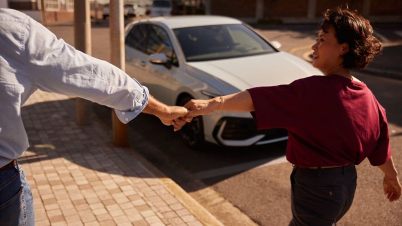 Un couple se tient par la main devant la VW Golf.