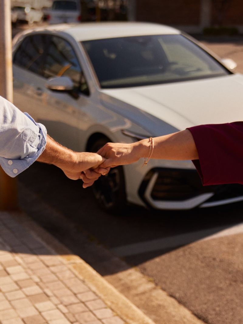 Un couple se tient par la main devant la VW Golf.