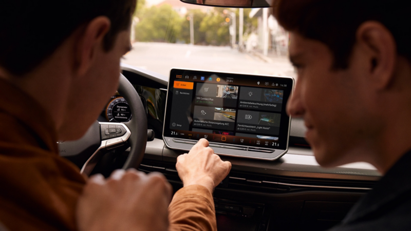 Innenansicht des VW Golf mit Blick auf das Display. Männer auf Fahrersitz und Beifahrersitz bedienen das Infotainment-System.
