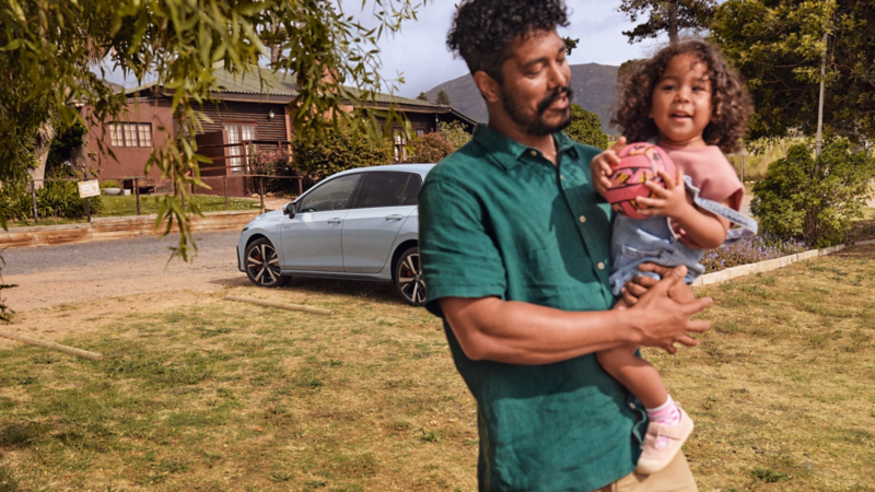 Un homme tenant une petite fille dans les bras se tient devant une VW Golf GTE blanche