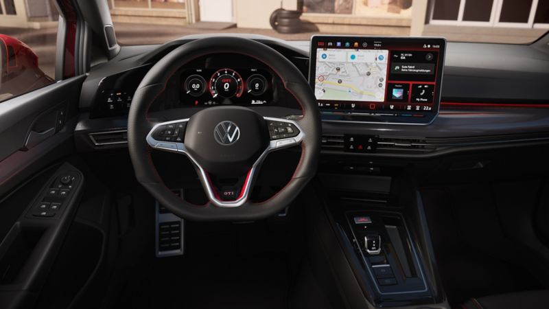 Interior view of the VW Golf showing the large display. A man is sitting in the front passenger seat and looking towards the driver seat smiling.