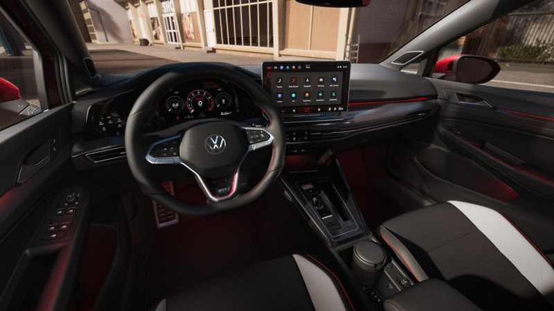 Interior view of the VW Golf with view of the driver, the cockpit and the large display. A man is sitting at the steering wheel and another man is in front of the car.