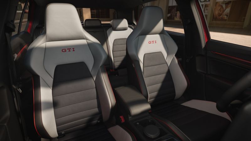 Vue des sièges avant d’une VW Golf GTI rouge avec la porte du conducteur ouverte. Une femme regarde dans la voiture.