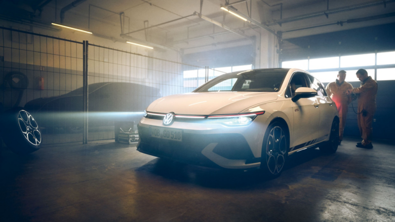 Vue de 2/4 avant de la Golf GTI Clubsport dans un stand, avec des rayons lumineux envoyés par les phares.